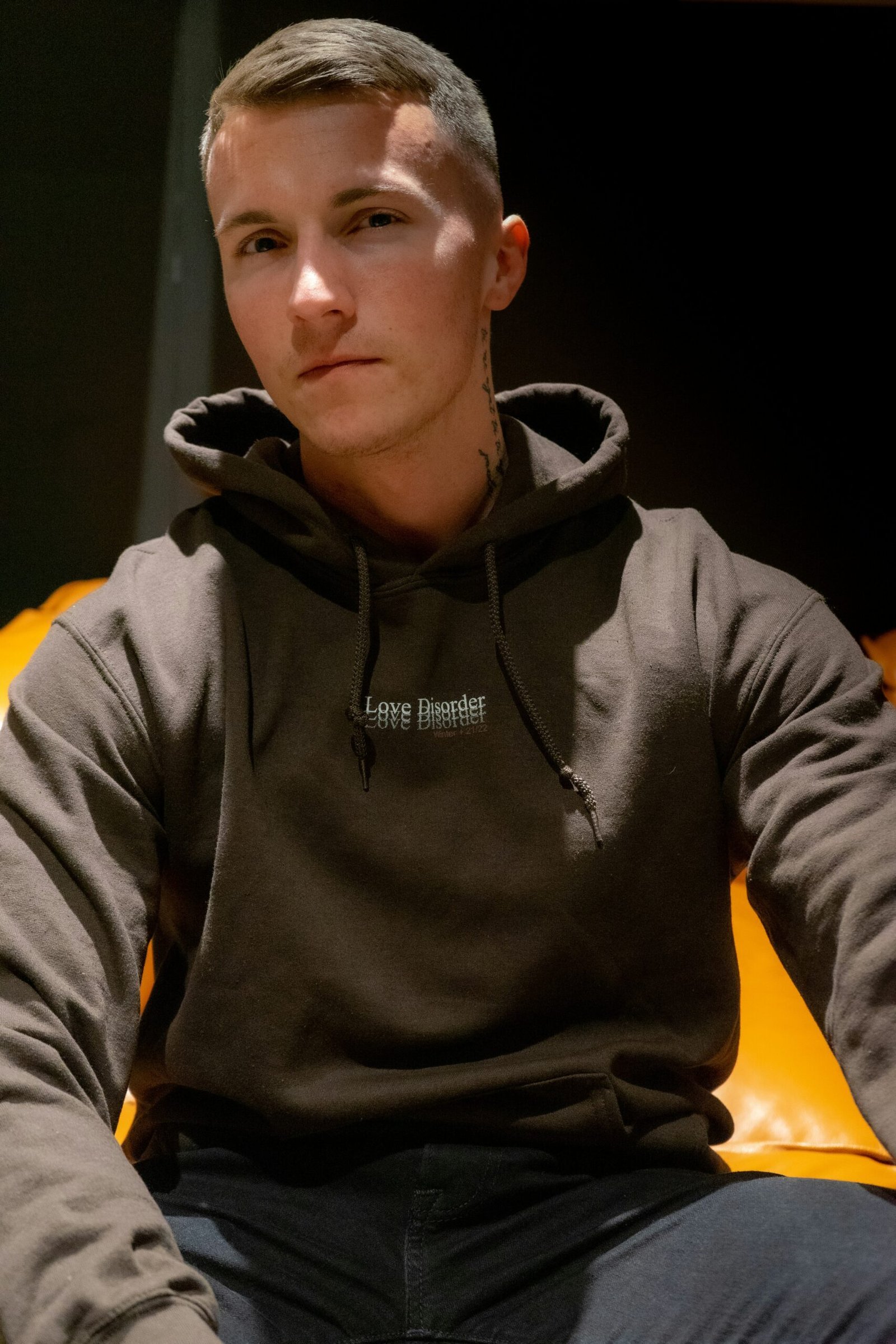 a young man sitting on a couch wearing a hoodie